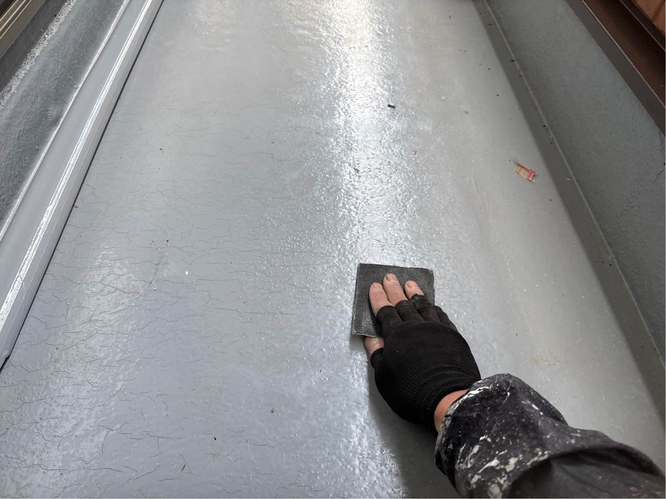 <strong>ベランダ床防水 下地処理中</strong><br>「ケレン作業」汚れや旧塗膜等による凹凸が有る場合、ムラなく均一な仕上がりにするため、下地を滑らかに整えています。この後「脱脂」も行います。既存の防水面に油分が残っていると新しい防水層が密着しないので、塗装前に脱脂の下地処理をしています。